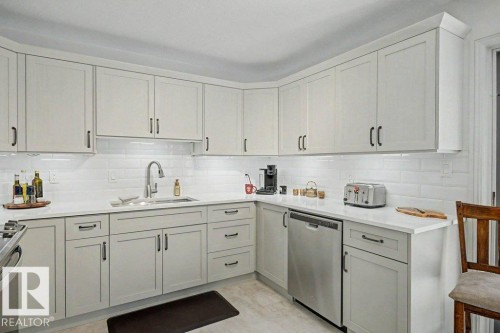 Modern kitchen featuring light-toned cabinetry with dark hardware, white subway tile backsplash, and light countertops - #39 2419 133 Av Nw, Edmonton, AB - Indoor Photo Showing Kitchen With Upgraded Kitchen