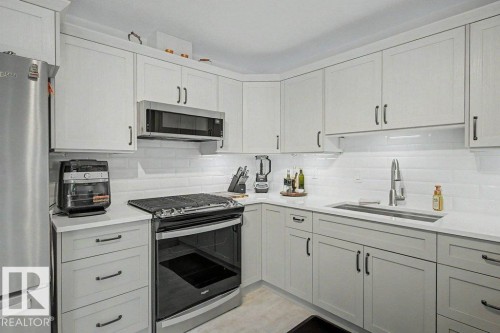 Contemporary kitchen featuring light-toned cabinetry, stainless steel appliances, a white subway tile backsplash, and a large single-basin sink with a pull-down faucet - #39 2419 133 Av Nw, Edmonton, AB - Indoor Photo Showing Kitchen With Upgraded Kitchen