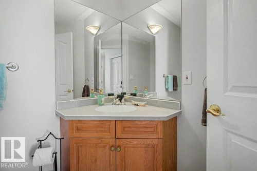 Bathroom vanity featuring a light wood-finish cabinet with brass-tone hardware, a light-toned countertop, and an integrated sink - #39 2419 133 Av Nw, Edmonton, AB - Indoor Photo Showing Bathroom