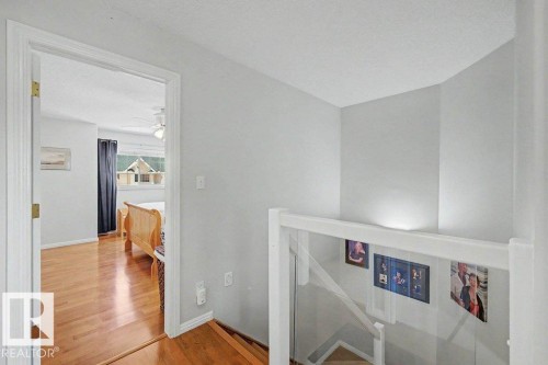 Light-filled interior featuring wood-finish flooring, a white ceiling fan, white trim, a window with dark drapes, and a glass panel railing - #39 2419 133 Av Nw, Edmonton, AB - Indoor Photo Showing Other Room