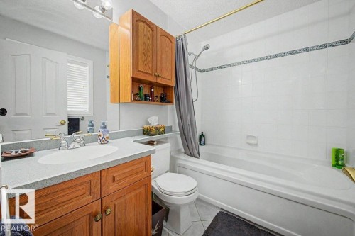 Full bathroom featuring a single vanity with wood-finish cabinetry, a light-toned countertop, and an integrated sink - #39 2419 133 Av Nw, Edmonton, AB - Indoor Photo Showing Bathroom