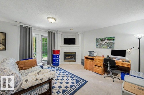 Corner fireplace with tiled surround, light-colored carpeting, recessed lighting, and a glass-paned door - #39 2419 133 Av Nw, Edmonton, AB - Indoor Photo Showing Other Room With Fireplace