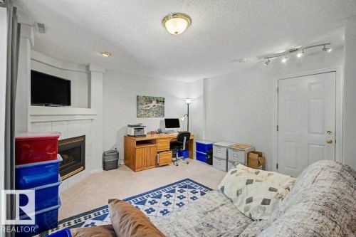 Carpeted interior space featuring a tiled fireplace with mantel, ceiling-mounted lighting, recessed lighting, and a paneled door - #39 2419 133 Av Nw, Edmonton, AB - Indoor Photo Showing Bedroom With Fireplace
