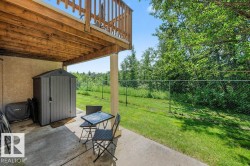 Covered concrete patio area featuring a storage shed, wood deck structure, and fenced yard with mature foliage - 
