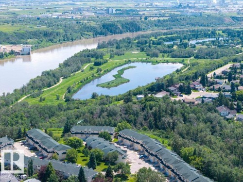 Aerial perspective showcasing multiple townhouse-style properties with dark shingle roofs, surrounded by mature green trees - #39 2419 133 Av Nw, Edmonton, AB - Outdoor With Body Of Water With View