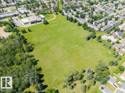 Expansive green space featuring manicured lawns, mature evergreen trees, and recreational goals - 