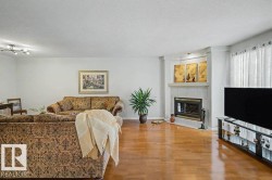 Living area featuring wood-finish flooring, a corner fireplace with a tile surround and mantel, and white walls - 