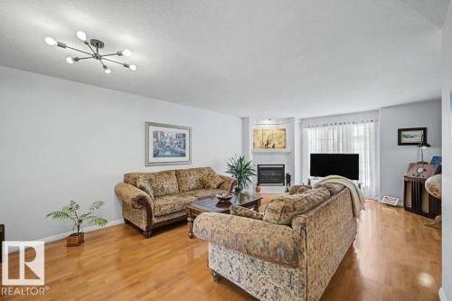 Bright living area featuring wood-finish flooring and a contemporary sputnik-style ceiling fixture - #39 2419 133 Av Nw, Edmonton, AB - Indoor Photo Showing Living Room With Fireplace