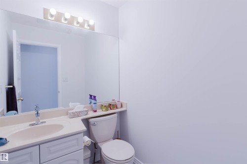 Bathroom vanity with an integrated sink and light-toned countertop, featuring white cabinetry and a large mirror with overhead vanity lighting - 15 Cormack Crescent Nw, Edmonton, AB - Indoor Photo Showing Bathroom