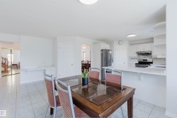 Bright dining area featuring tile flooring, a built-in desk, and an open-concept kitchen with white cabinetry and a breakfast bar - 