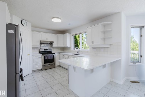 Kitchen featuring white cabinetry, stainless steel appliances, a white tile backsplash, and light-toned countertops - 15 Cormack Crescent Nw, Edmonton, AB - Indoor Photo Showing Kitchen