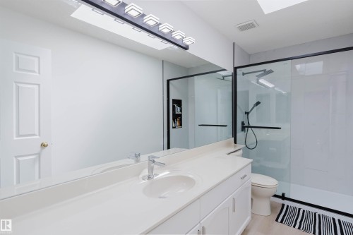 Modern bathroom featuring a single vanity with a white countertop and undermount sink, a large wall-mounted mirror, and a glass-enclosed shower with matte black fixtures - 15 Cormack Crescent Nw, Edmonton, AB - Indoor Photo Showing Bathroom