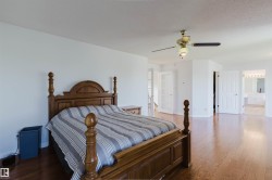 Spacious room featuring wood-finish flooring, a ceiling fan with integrated lighting, and multiple white doors - 