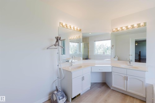 Spacious bathroom featuring light wood-finish flooring, dual vanity sinks, white cabinetry, integrated countertop, and large wall-mounted mirrors with overhead lighting - 15 Cormack Crescent Nw, Edmonton, AB - Indoor Photo Showing Bathroom