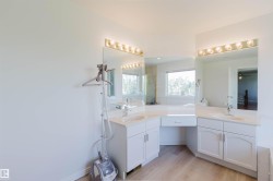 Spacious bathroom featuring light wood-finish flooring, dual vanity sinks, white cabinetry, integrated countertop, and large wall-mounted mirrors with overhead lighting - 