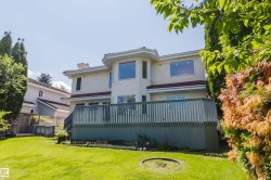 Rear exterior featuring a stucco finish, a substantial deck with a wood railing, and a manicured lawn - 