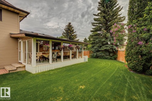 Expansive green lawn with mature trees, complementing a covered patio featuring a glass railing and direct access to the home's exterior siding - 15804 80 Street Nw, Edmonton, AB - Outdoor