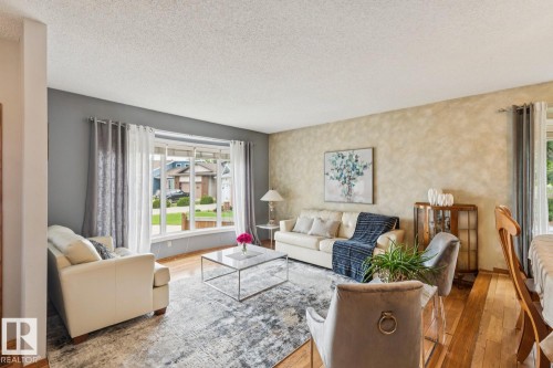 Living area featuring wood-finish flooring, a large picture window with white trim, and a textured accent wall - 15804 80 Street Nw, Edmonton, AB - Indoor Photo Showing Living Room
