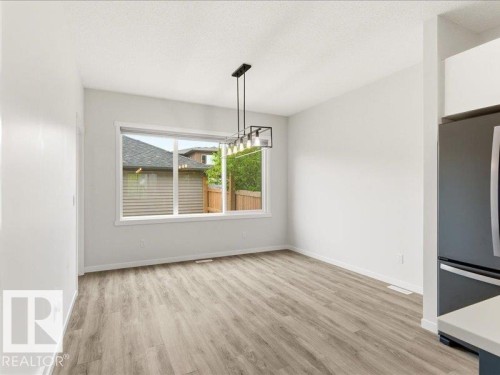 Open-concept dining area featuring light wood-finish flooring, a contemporary linear chandelier with exposed bulbs, and a large window providing natural light - 17487 77 Street, Edmonton, AB - Indoor