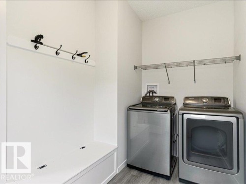 Dedicated utility space featuring light-toned walls, wood-finish flooring, a built-in bench with storage, a wall-mounted coat rack, and an overhead wire shelf - 17487 77 Street, Edmonton, AB - Indoor Photo Showing Laundry Room