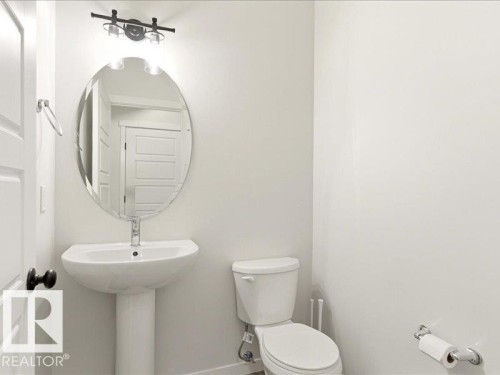 Powder room featuring a pedestal sink, oval mirror, and contemporary light fixture - 17487 77 Street, Edmonton, AB - Indoor Photo Showing Bathroom