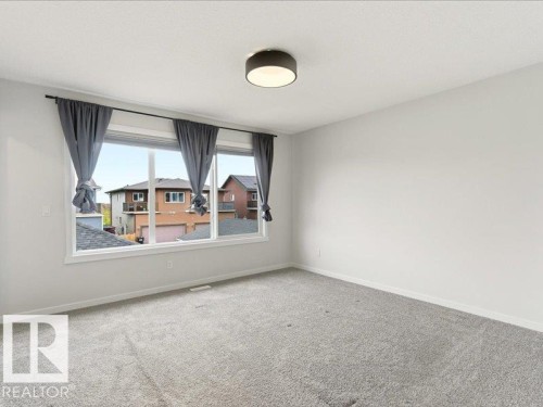 Bright room featuring a large multi-pane window, light gray carpeting, neutral wall paint, and a contemporary flush-mount ceiling light - 17487 77 Street, Edmonton, AB - Indoor Photo Showing Other Room