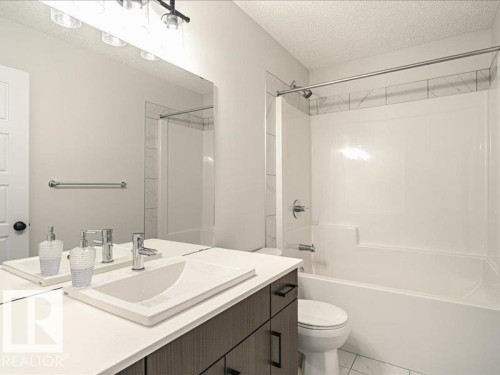 Bathroom featuring a white integrated sink with chrome faucet, a wood-finish vanity with dark hardware, and a tub-shower combination with partial tile surround - 17487 77 Street, Edmonton, AB - Indoor Photo Showing Bathroom