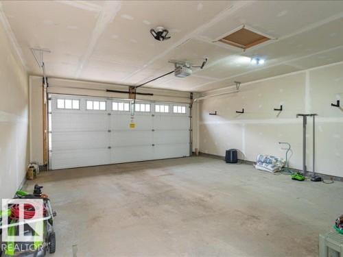 Spacious garage featuring a white panel garage door with upper window inserts, an automatic garage door opener, a concrete floor, and multiple wall-mounted hooks - 17487 77 Street, Edmonton, AB - Indoor Photo Showing Garage