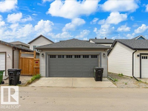 Detached garage featuring light gray siding, dark gray overhead door with window inserts, and sconce lighting - 17487 77 Street, Edmonton, AB - Outdoor