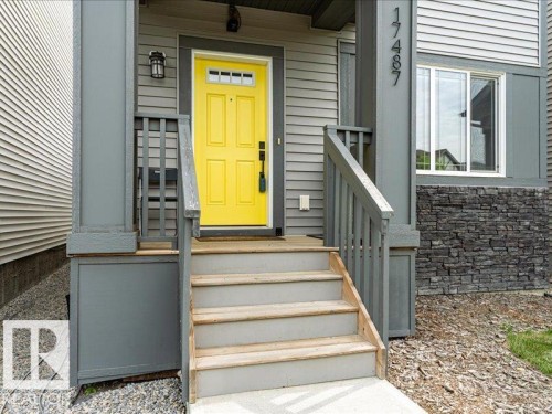 Exterior entry featuring a vibrant yellow door with transom window detail, gray siding, and stone-finish foundational accents - 17487 77 Street, Edmonton, AB - Outdoor With Exterior