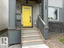 Exterior entry featuring a vibrant yellow door with transom window detail, gray siding, and stone-finish foundational accents - 17487 77 Street, Edmonton, AB  - Outdoor With Exterior 