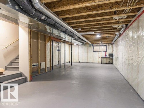 Expansive unfinished basement featuring a painted concrete floor, exposed ceiling joists, and a partial staircase with a wooden handrail - 17487 77 Street, Edmonton, AB - Indoor Photo Showing Basement