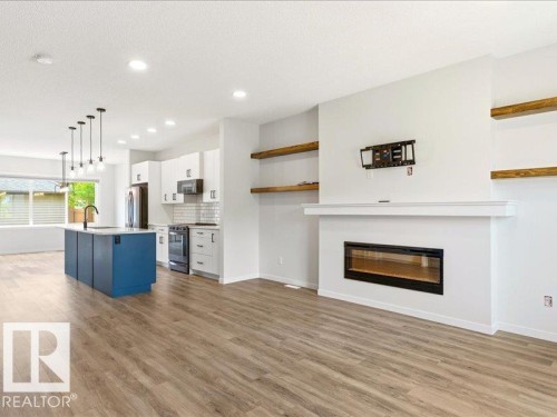 Open-concept living space featuring wood-finish flooring, a modern electric fireplace, and floating wood shelves - 17487 77 Street, Edmonton, AB - Indoor With Fireplace