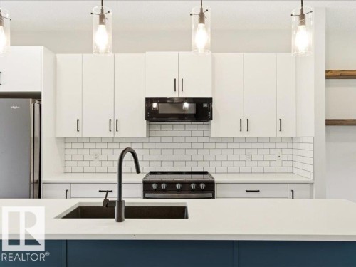 Modern kitchen featuring white shaker-style cabinetry, white subway tile backsplash, and a large central island with a built-in sink and matte black faucet - 17487 77 Street, Edmonton, AB - Indoor Photo Showing Kitchen With Upgraded Kitchen