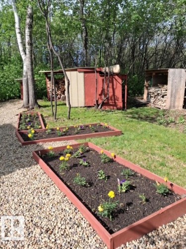 Outdoor garden area featuring multiple raised garden beds with planted flowers, a gravel path, and a grass lawn - 204 Sandy Beach Way, Rural Two Hills County, AB - Outdoor