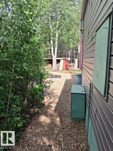Gravel pathway alongside the property, bordered by extensive mature greenery - 204 Sandy Beach Way, Rural Two Hills County, AB - Outdoor