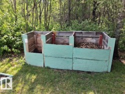 Three-bin compost system featuring painted wood construction, integrated into a natural, treed setting - 