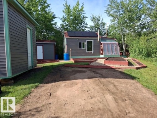 Gravel driveway providing access to two structures featuring dark grey siding with light green trim - 204 Sandy Beach Way, Rural Two Hills County, AB - Outdoor
