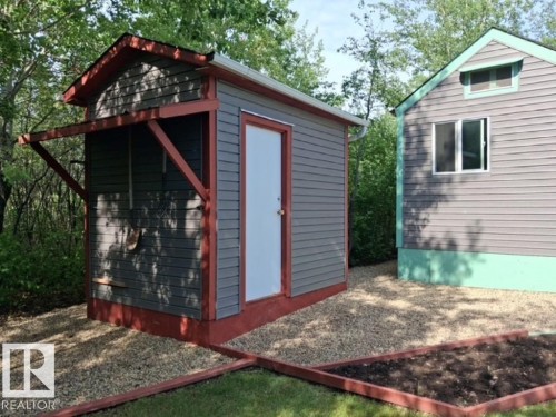 Gravel landscaping surrounding a gray utility building with a white entry door and a covered side storage area - 204 Sandy Beach Way, Rural Two Hills County, AB - Outdoor With Exterior