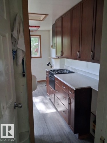 Efficient kitchen featuring wood-finish cabinetry, light-toned countertops, a built-in range, and wood-finish flooring - 204 Sandy Beach Way, Rural Two Hills County, AB - Indoor