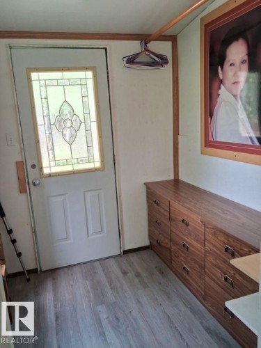 Entryway featuring a white door with decorative glass inlay, wood-finish flooring, built-in storage cabinetry with dark hardware, and a hanging rod - 204 Sandy Beach Way, Rural Two Hills County, AB - Indoor Photo Showing Other Room