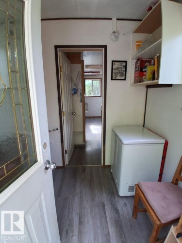 Interior entryway featuring wood-finish flooring, a white paneled door with decorative glass, white walls, and an overhead built-in storage cabinet - 204 Sandy Beach Way, Rural Two Hills County, AB - Indoor Photo Showing Laundry Room