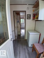 Interior entryway featuring wood-finish flooring, a white paneled door with decorative glass, white walls, and an overhead built-in storage cabinet - 