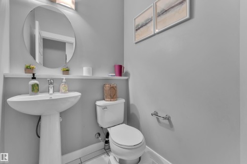 Pedestal sink with chrome faucet, circular mirror, and wall-mounted lighting - 1942 Chapman Road Sw, Edmonton, AB - Indoor Photo Showing Bathroom