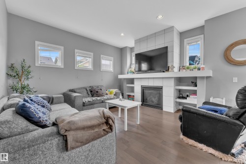 Living area featuring wood-finish flooring, a contemporary fireplace with tile surround, built-in shelving, recessed lighting, and multiple windows - 1942 Chapman Road Sw, Edmonton, AB - Indoor Photo Showing Living Room With Fireplace