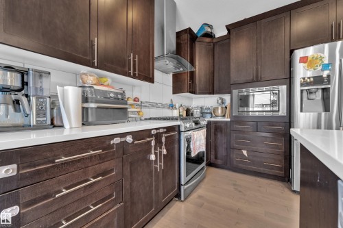 Kitchen featuring dark wood-finish cabinetry, white countertops, and stainless steel appliances, including a built-in microwave, range, and refrigerator - 1942 Chapman Road Sw, Edmonton, AB - Indoor Photo Showing Kitchen With Upgraded Kitchen