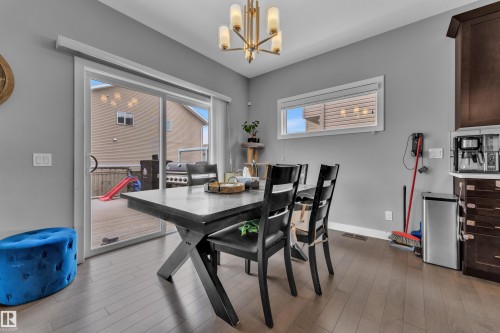 Dining area featuring wood-finish flooring, a contemporary chandelier, and a sliding glass door providing access to an outdoor deck - 1942 Chapman Road Sw, Edmonton, AB - Indoor Photo Showing Dining Room