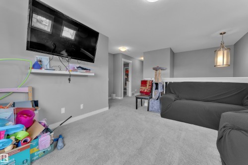 Carpeted loft area featuring a mounted television, a floating wall shelf, and a partial balustrade - 1942 Chapman Road Sw, Edmonton, AB - Indoor