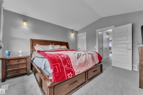 Vaulted ceiling bedroom featuring wall-mounted sconces, wood-finish bed frame with built-in storage drawers, and gray wall paint - 1942 Chapman Road Sw, Edmonton, AB - Indoor Photo Showing Bedroom