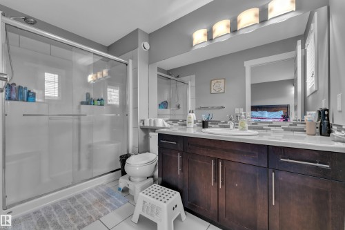 Bathroom featuring a clear glass shower enclosure, a dark wood-finish vanity with a white countertop, a rectangular undermount sink, and a large wall-mounted mirror - 1942 Chapman Road Sw, Edmonton, AB - Indoor Photo Showing Bathroom